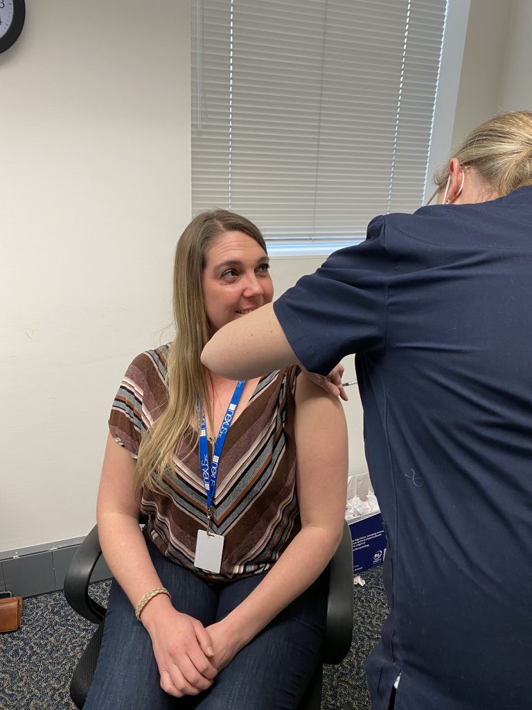 Nexus staff member smiles as she receives her first dose of COVID19 vaccination from a nurse.