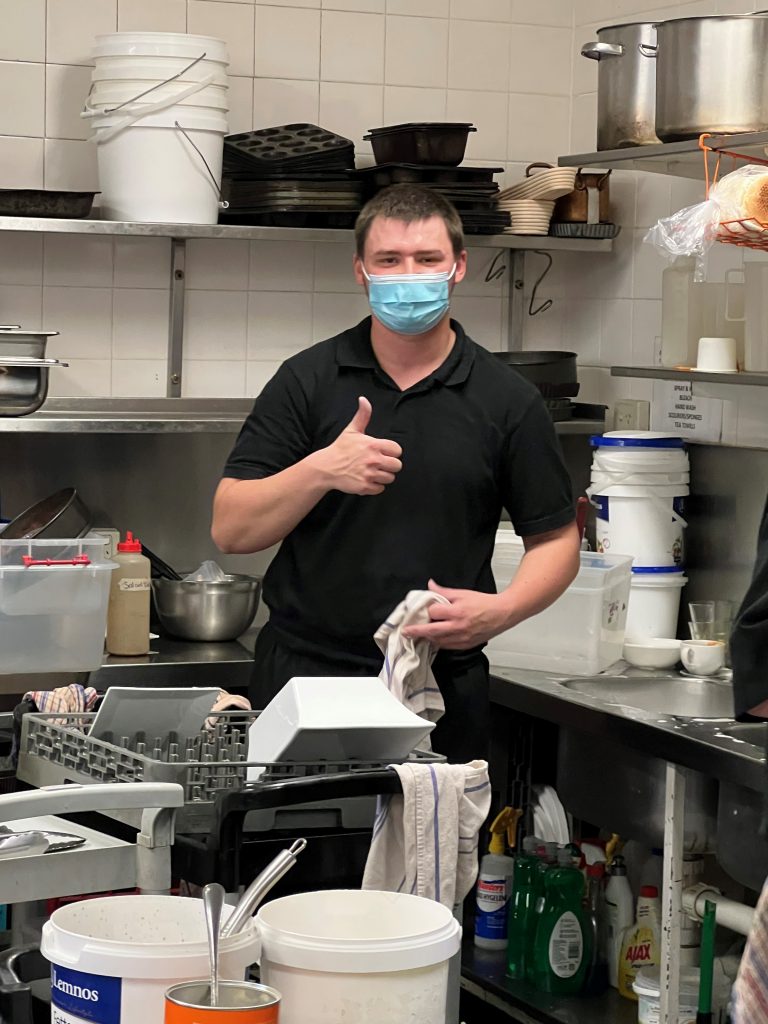 Customised Employment Client, Jack, washing dishes in cafe kitchen